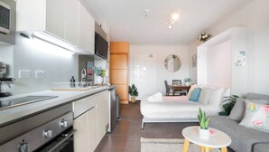 A modern kitchen with stainless steel appliances, a dining area with a sofa and table, and a small balcony with a potted plant. - Beautiful Studio with City Views in Randwick (Randwick)