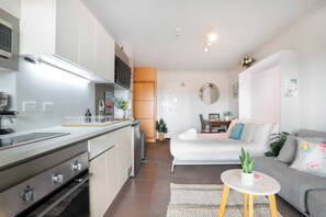 Eine moderne Küche mit Edelstahlgeräten, ein Essbereich mit einer Couch und einem Tisch sowie ein kleiner Balkon mit einem Blumentopf.
