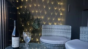 A wicker lounge area with a glass table, a bottle of wine, and a glass. - Beautiful Studio with City Views in Randwick (Randwick)