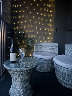 Eine Lounge-Ecke aus Korbmöbeln mit einem Glastisch, einer Weinflasche und einem Weinglas.