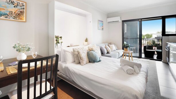 Une chambre moderne avec un lit, un bureau et un balcon doté d’un espace salon extérieur.