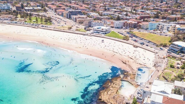 An aerial view of a coastal town with a wide sandy beach, a rocky shoreline, and residential buildings. - Beautiful Studio with City Views in Randwick (Randwick)
