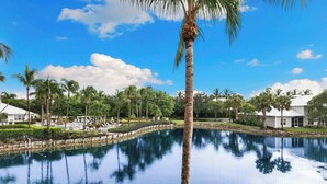 Ein strahlend blauer Himmel, ein ruhiger Pool, der Palmen wider spiegelt, und ein weißes Gebäude mit überdachtem Bereich.
