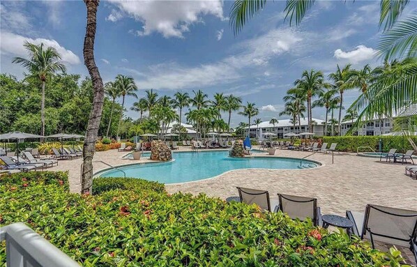 A pool area with lounge chairs, palm trees, and a clear sky. - Lakeview 2 BDRM Naples Condo l Walk to Amenities (Naples)