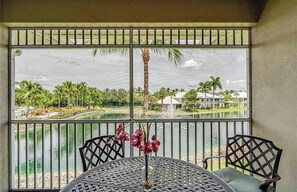 A view from a balcony with a table and chairs, overlooking a body of water and a building with a white roof. - Lakeview 2 BDRM Naples Condo l Walk to Amenities (Naples)
