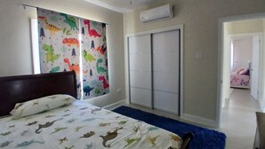 Quarto com cama, ventoinha no teto, guarda-roupa e janela com cortinas de tema dinossauros.