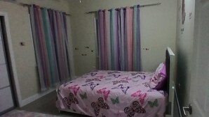 Quarto com cama, cortinas, ventoinha no teto e tapete colorido.