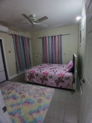 Ein Schlafzimmer mit Bett, Vorhängen, Deckenventilator und einem farbenfrohen Teppich.