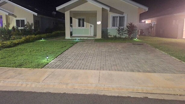 Uma casa de dois andares com entrada pavimentada e gramado bem cuidado.