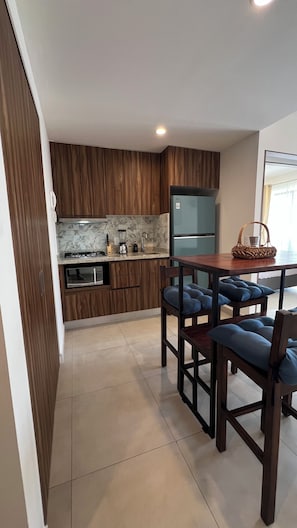 A modern kitchen with wooden cabinets, a marble backsplash, and a built-in oven. There is a dining area with a wooden table and blue cushioned chairs. - Vallarta Style: Cozy, Central and Safe Apartment (Puerto Vallarta)