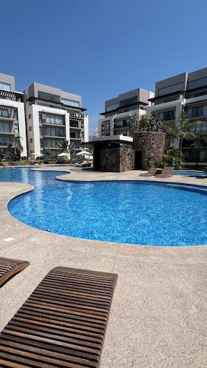 A swimming pool with a stone wall and lounge chairs, surrounded by modern buildings. - Vallarta Style: Cozy, Central and Safe Apartment (Puerto Vallarta)
