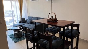Un salon moderne comprenant un coin repas, un canapé, un téléviseur fixé au mur et un balcon agrémenté de rideaux.
