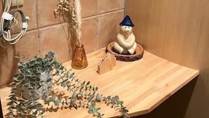 Ein Holztresen mit einer kleinen Bärenfigur, einer Vase mit getrockneten Pflanzen und einer Pflanze mit grünen Blättern.
