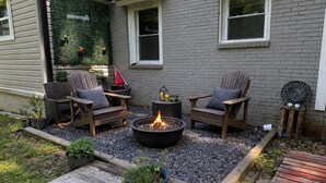 Ein Patio mit Feuerstelle, zwei Holzstühlen und einem kleinen Tisch.