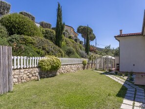 Ein gepflegter Garten mit Steinmauer, Holzzaun und einem Weg zu einem Gebäude.