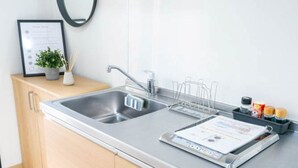 Una cocina moderna con un lavamanos de acero inoxidable, armarios de madera, un microondas y una pequeña planta en maceta.
