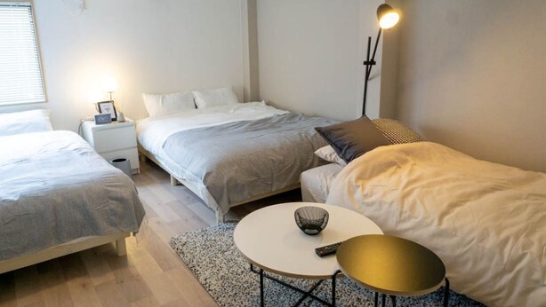 Un dormitorio con dos camas, una mesita de noche con lámpara, una mesa redonda con un cuenco y un equipo de aire acondicionado en la pared.