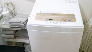 Una lavadora blanca y compacta con panel de control, una pequeña mesa con toallas dobladas y una silla.