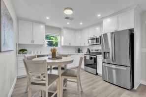 Una cucina moderna con mobili bianchi, elettrodomestici in acciaio inossidabile e una zona pranzo con tavolo e sedie rotonde.