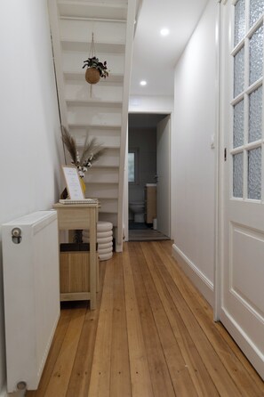 A hallway with wooden flooring, a radiator, a small table with a sign, and a door with frosted glass panels.