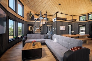 Un vaste espace de vie comprenant un grand canapé d’angle, une table basse en bois et un escalier menant à l’étage supérieur.
