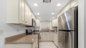 A kitchen with white cabinets, a stainless steel refrigerator, a microwave, and a stove. - Oasis 21 (Daytona Beach)