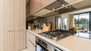 Une cuisine moderne équipée d’une cuisinière à gaz, d’appareils électroménagers en acier inoxydable et d’une grande fenêtre offrant une vue sur l’extérieur.