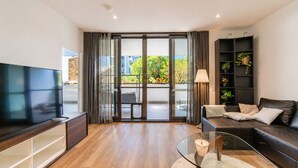 Una sala moderna con una televisión de pantalla plana, una mesa de centro de vidrio, un sofá, una estantería y un ventanal corredero que da a un espacio exterior.
