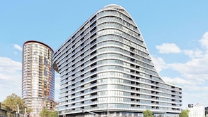 Ein modernes, mehrstöckiges Hotel mit geschwungener Fassade, zahlreichen Balkonen und einer markanten Glasfront.