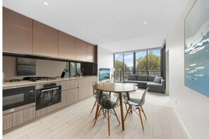 Eine moderne Küche mit integrierten Geräten, eine Essecke mit rundem Tisch und Stühlen, und ein großes Fenster mit Blick ins Freie.