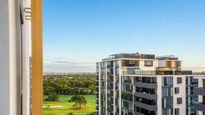 A high-rise building with multiple balconies and large windows, overlooking a green landscape with trees and a golf course. - Eastgardens 2BR/2BA | 2 Parking + Shops (Eastgardens)