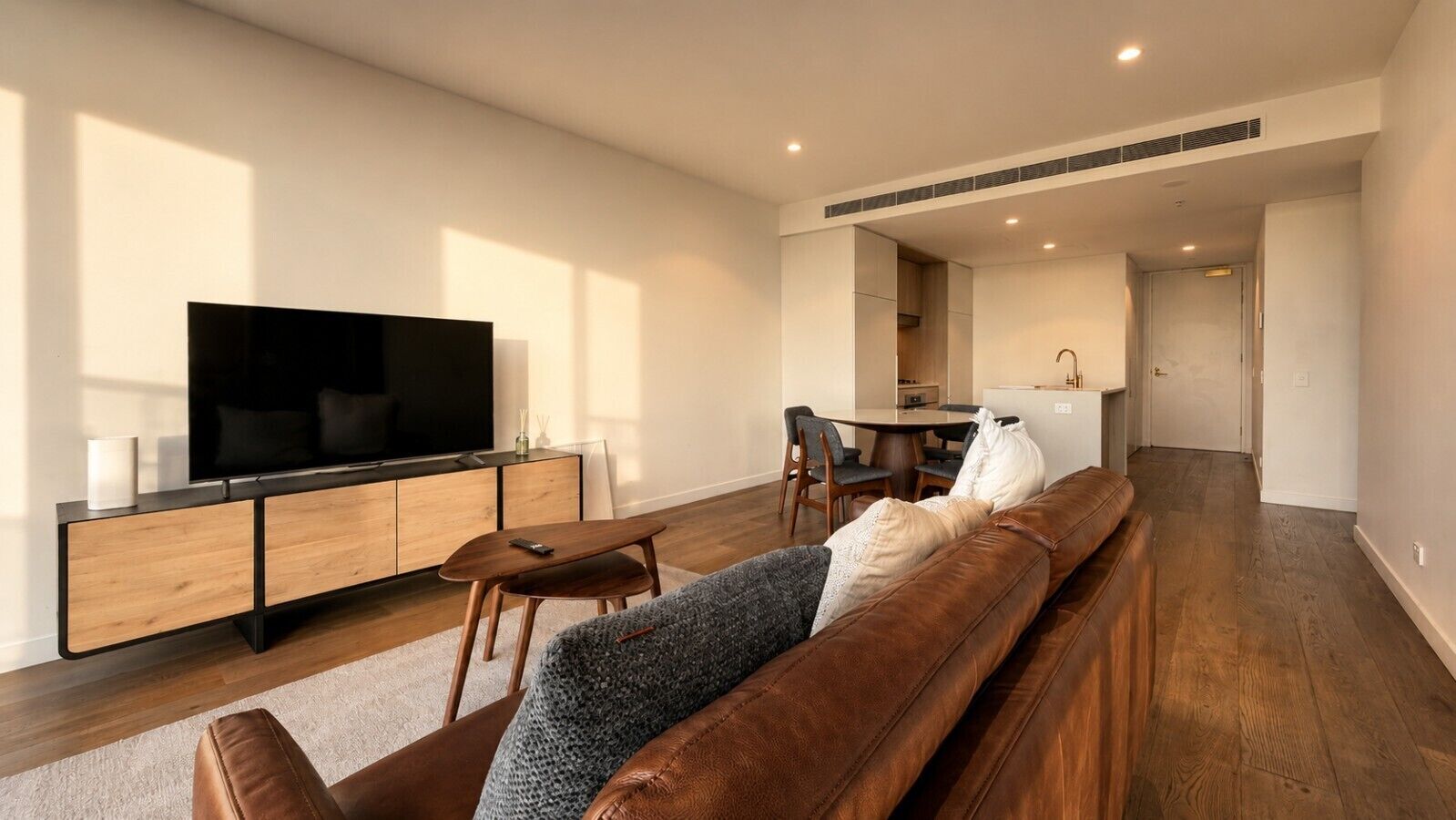 A modern living room with a flat-screen TV, wooden furniture, and a sofa.