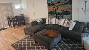 Un salón con sofá modular, reposapiés y un tapiz en la pared.