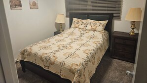 Un dormitorio con cama, mesita de noche, lámpara y dos cuadros en la pared.