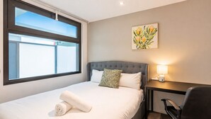 Una habitación de hotel con cama, escritorio, silla, ventana y un cuadro en la pared.