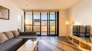 Una sala de estar moderna con un sofá, una mesa de centro, un televisor y un ventanal corredizo que da a un balcón.
