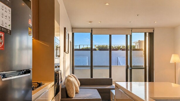 Una cocina moderna con refrigerador integrado, una zona de comedor con sofá y mesa, y ventanas amplias que ofrecen vistas a la ciudad.