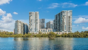 A high-rise residential building with multiple balconies, situated by a body of water. - Wolli Creek 2BR | Station, Airport, Pool + Parking (Wolli Creek)