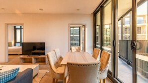 Ein modernes Wohnzimmer mit Fernseher, einem Esstisch mit Stühlen, einer Couch und einem Balkon mit Geländer.