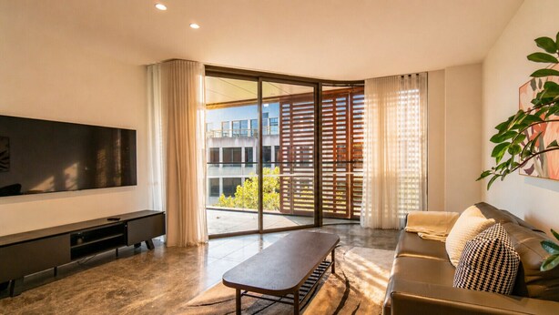 Ein modernes Wohnzimmer mit Flachbildfernseher, einer Couch, einem Couchtisch und einer Glastür zum Balkon.