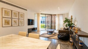 A modern living room with a dining area, a flat-screen TV, and a large window with blinds. - 2BR by Circular Quay | The Rocks + Free Parking (The Rocks)