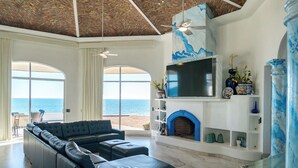Ett modernt vardagsrum med en stor hörnsoffa, en öppen spis, en tv och utsikt över havet.