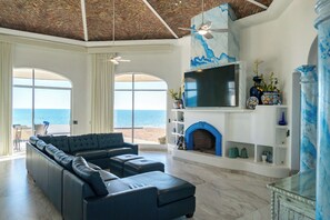 Ein modernes Wohnzimmer mit einer großzügigen Eckcouch, einem Kamin, einem Fernseher und Blick aufs Meer.