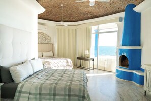 Ein Schlafzimmer mit Bett, Deckenventilator, Meerblick und Kamin mit blauen Fliesen.