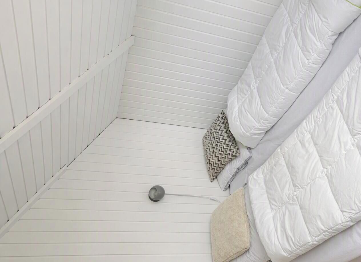 A white room with a bed, a patterned pillow, and a small round object on the floor.
