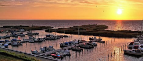 A marina with boats docked, a dock, and a sunset in the background.