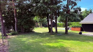 Un pati amb gespa, arbres, una estructura de fusta i una porta metàl·lica.