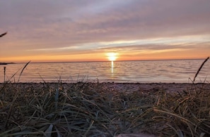 Ein Sonnenuntergang über ruhigem Wasser, im Vordergrund Gras.