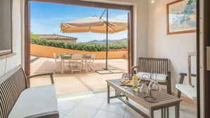 An open-plan living area with a patio, a dining table with chairs, a sofa, and a small table with a bottle and glasses.