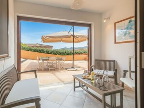 Ein offener Wohnbereich mit Terrasse, einem Esstisch mit Stühlen, einem Sofa und einem kleinen Tisch mit Flasche und Gläsern.